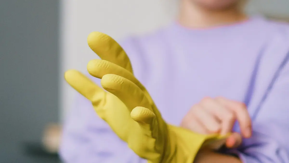 Homeowner putting on yellow rubber gloves indoors — the decision moment before beginning a DIY mold removal project at home