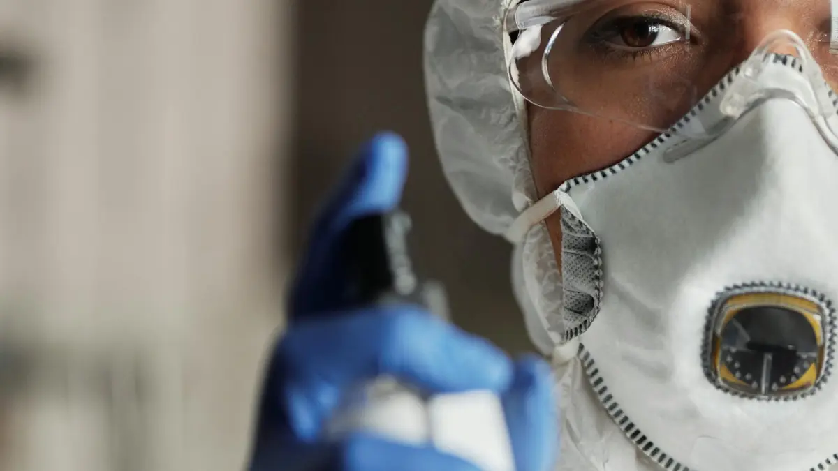 Person wearing full PPE including N95 respirator, face shield, and nitrile gloves holding an antimicrobial spray bottle — the correct protective setup for DIY mold removal