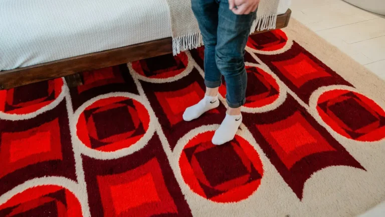 Dirty red carpet with dark discoloration patches and rolled backing exposing hidden mold in carpet damage.