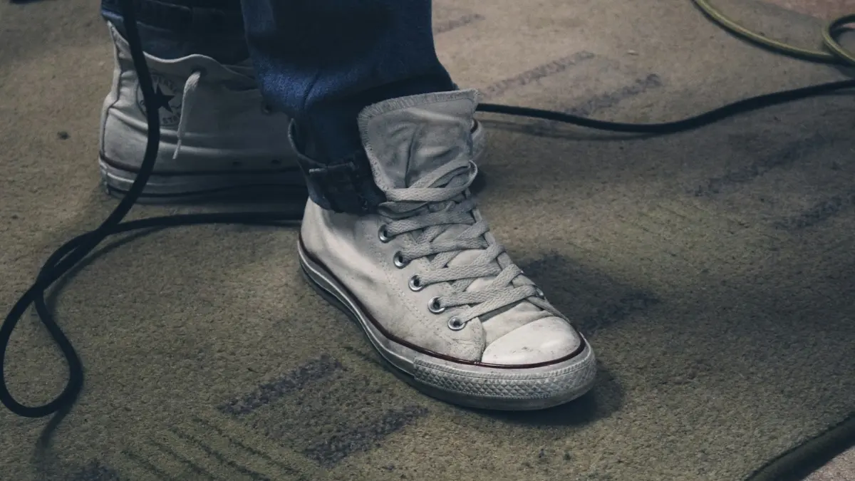 White sneakers standing on a stained beige carpet with dark spots showing visible mold in carpet contamination.