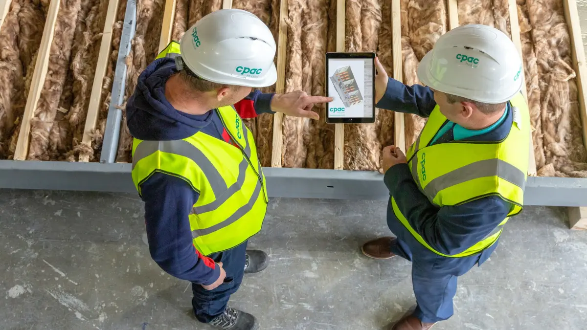 Two professional inspectors in hard hats reviewing building plans on a tablet during a mold inspection walkthrough.