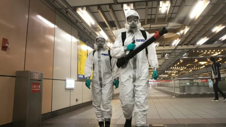 Workers in full hazmat Safety Gear with respirators preparing to disinfect a contaminated indoor space.